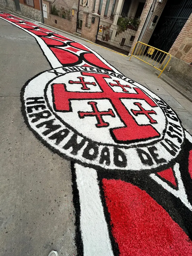 Alfombra del X aniversario de la Hermandad de la Santa Cruz en el Corpus Christi 2025 de Los Navalmorales, en blanco, rojo y negro