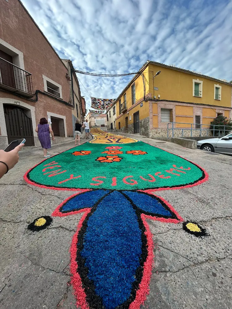 Alfombra en la calle Sagunto durante el Corpus Christi 2025 en Los Navalmorales, con mensaje "Ven y sígueme"