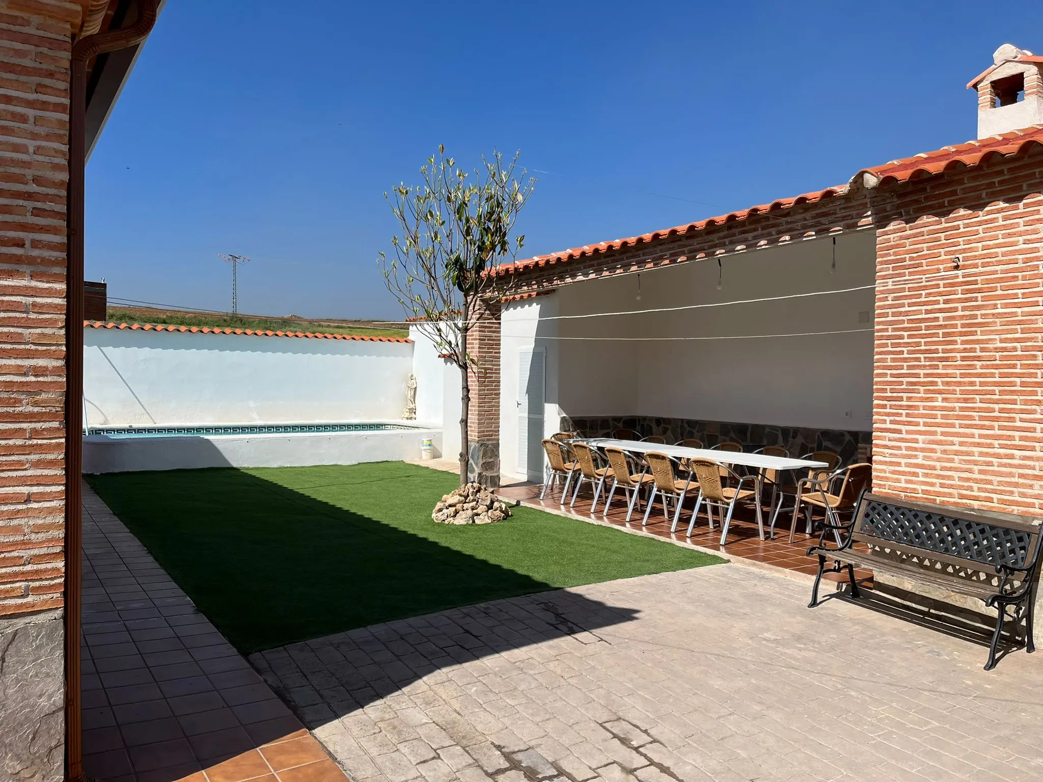 Zona ajardinada con piscina, mesas y sillas para comer al aire libre