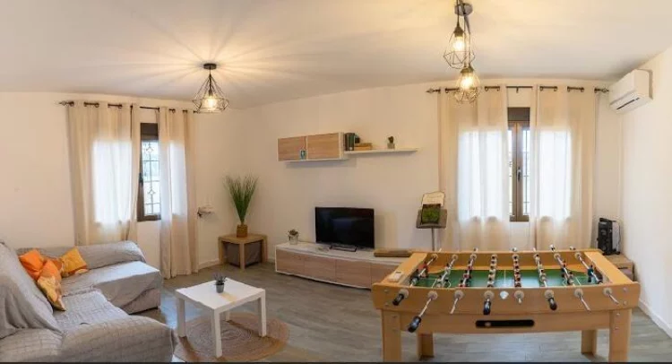 Salón acogedor con sofá, televisión, futbolín y luz natural en La Fragua del Sauce